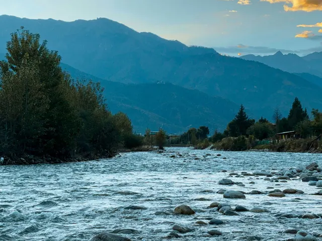 As dusk falls over Paro, Bhutan, a gentle river winds through rocky shallows beneath the silhouettes of forested hills a jigsaw puzzle
